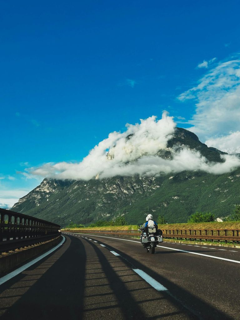 Un motociclista solitario recorre una pintoresca carretera con majestuosas montañas en Italia.